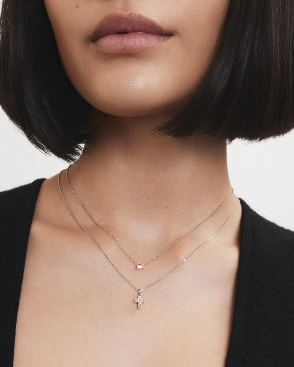 Image of model wearing white gold cross cut pendant layered with a white gold mini baguette cut pendant